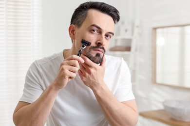 Photo of Handsome man shaving with razor in bathroom