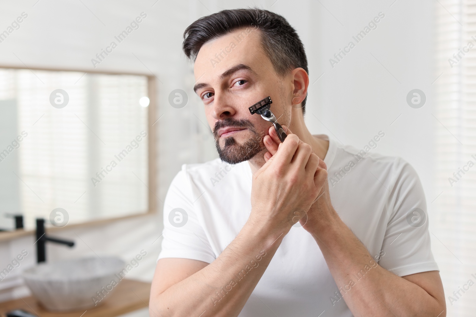 Handsome man shaving with razor in bathroom Photo of Handsome man shaving with razor in bathroom