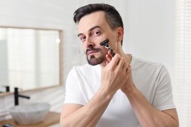 Photo of Handsome man shaving with razor in bathroom