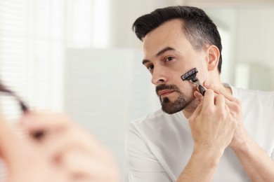 Photo of Handsome man shaving with razor near mirror at home