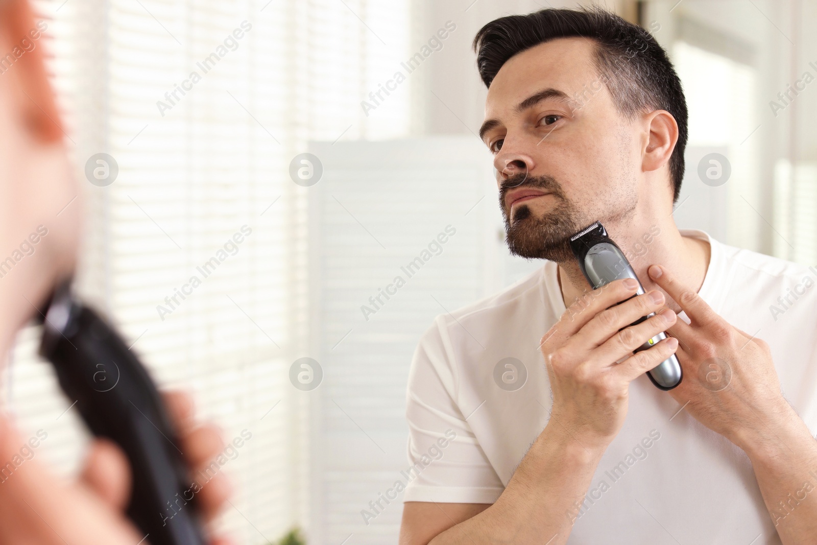 Handsome man shaving with trimmer near mirror at home Photo of Handsome man shaving with trimmer near mirror at home
