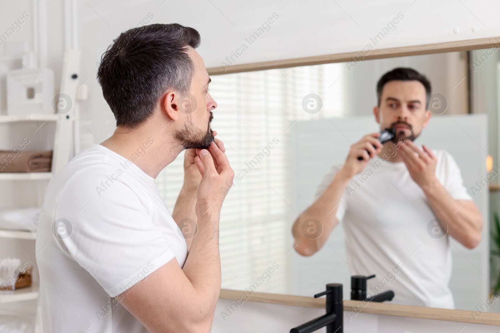 Handsome man shaving with trimmer near mirror at home, selective focus Photo of Handsome man shaving with trimmer near mirror at home, selective focus