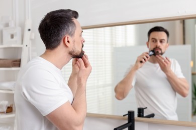 Photo of Handsome man shaving with trimmer near mirror at home, selective focus