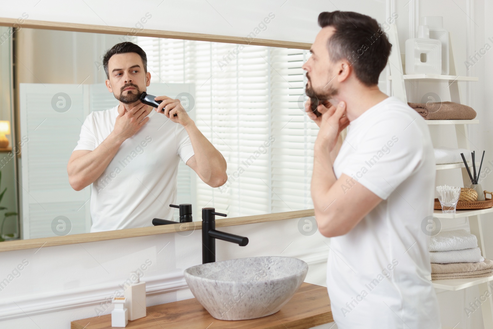 Handsome man shaving with trimmer near mirror at home Photo of Handsome man shaving with trimmer near mirror at home