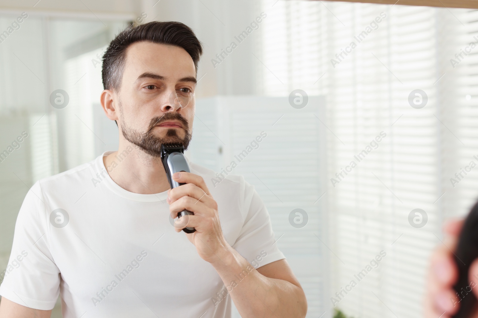 Handsome man shaving with trimmer near mirror at home Photo of Handsome man shaving with trimmer near mirror at home