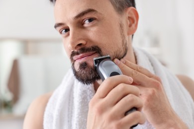 Photo of Handsome man shaving with trimmer at home, closeup