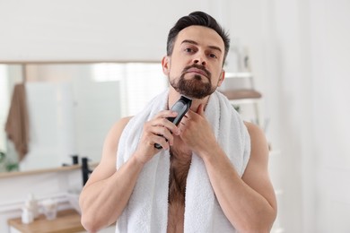 Photo of Handsome man shaving with trimmer in bathroom