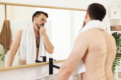 Photo of Handsome man before shaving looking at mirror in bathroom