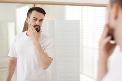 Photo of Handsome man before shaving looking at mirror in bathroom