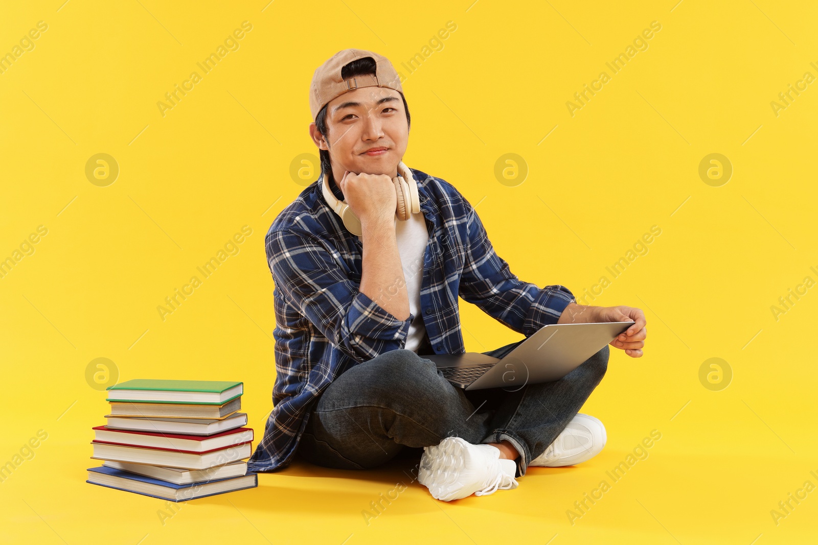 Student with headphones and laptop on orange background Photo of Student with headphones and laptop on orange background