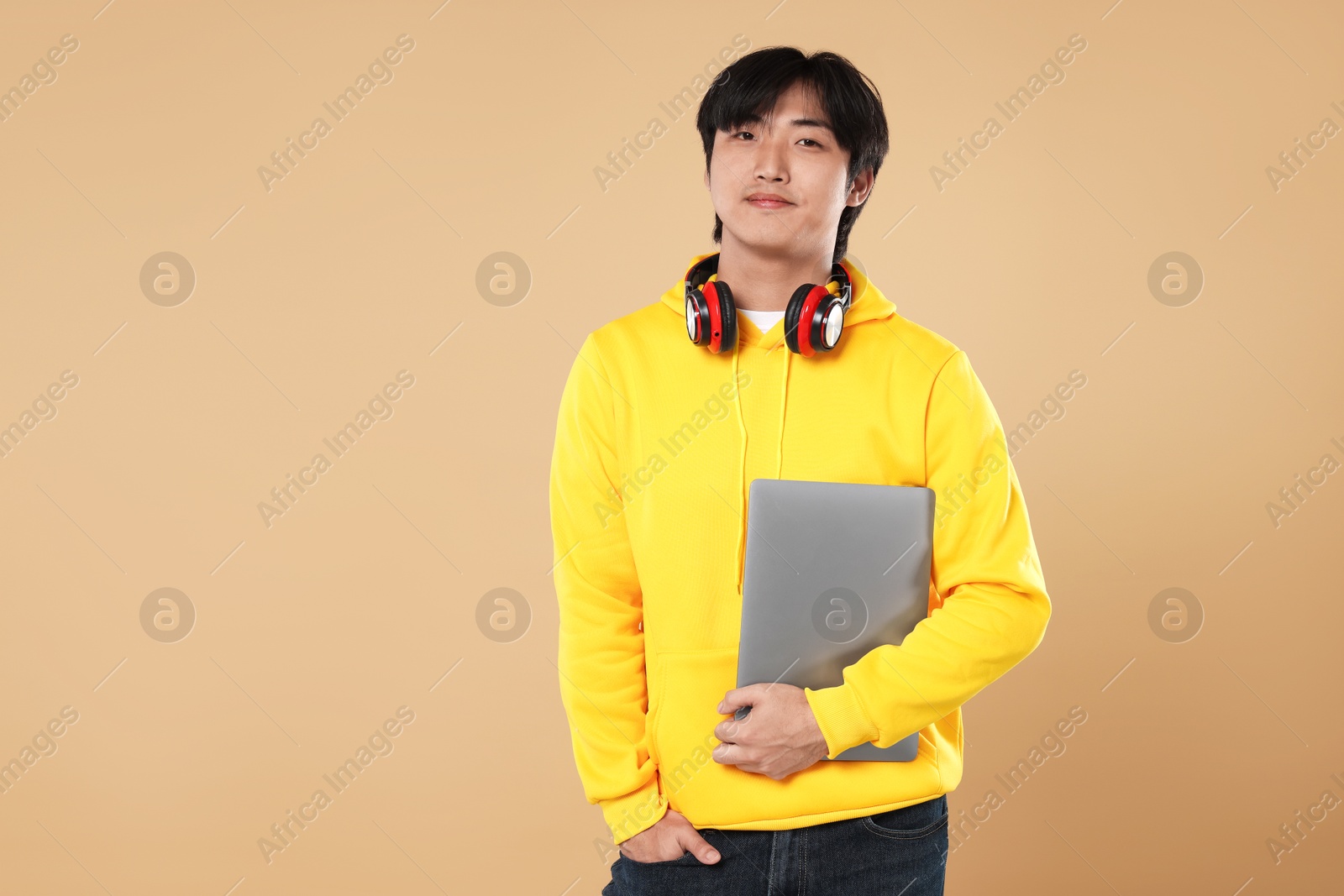 Student with headphones and laptop on beige background, space for text Photo of Student with headphones and laptop on beige background, space for text