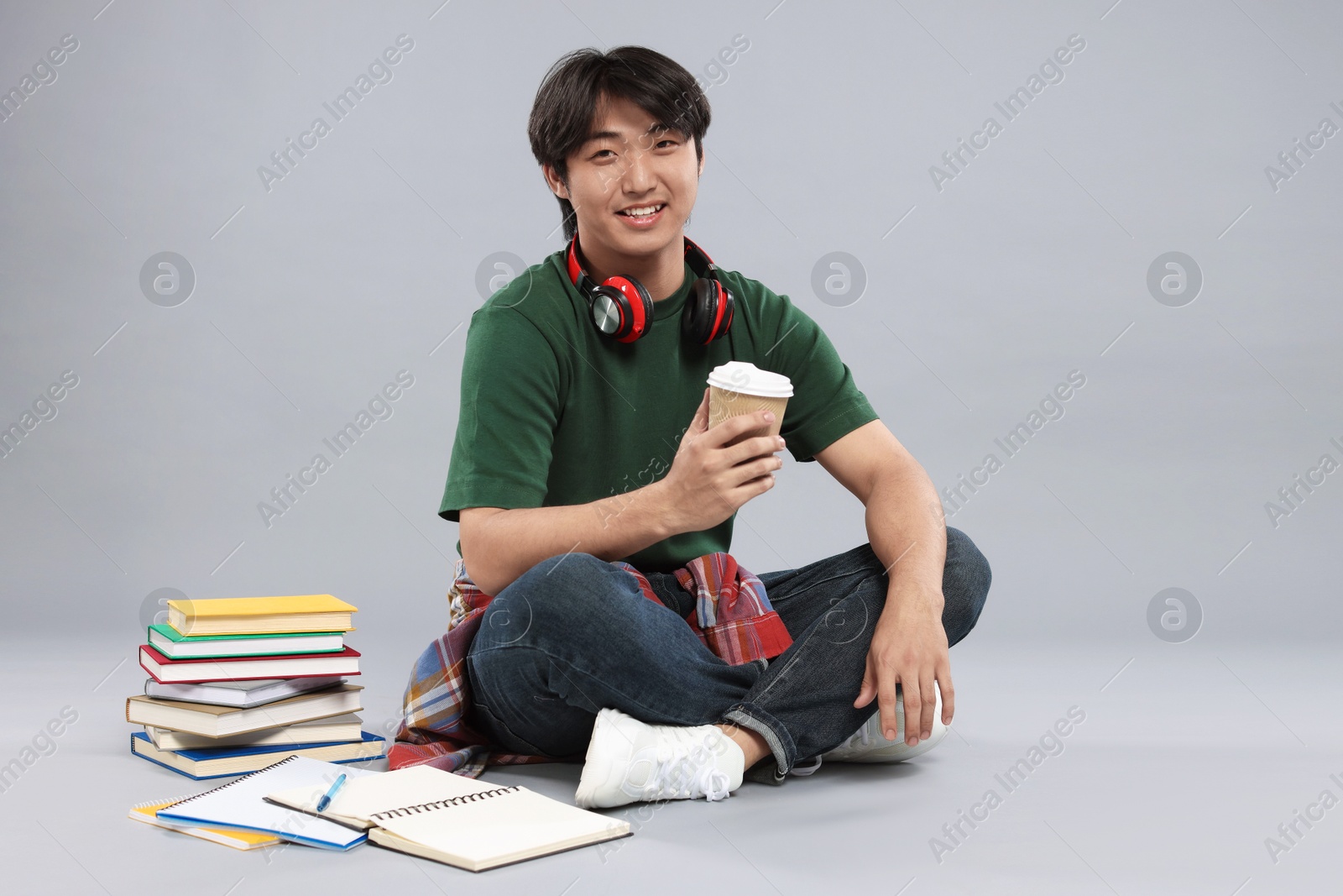 Student with headphones, coffee and books on grey background Photo of Student with headphones, coffee and books on grey background