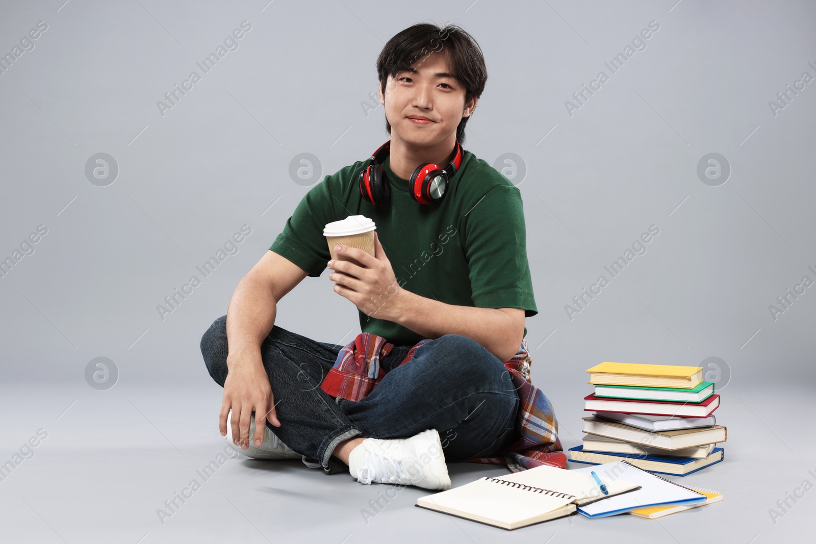 Student with headphones, coffee and books on grey background Photo of Student with headphones, coffee and books on grey background