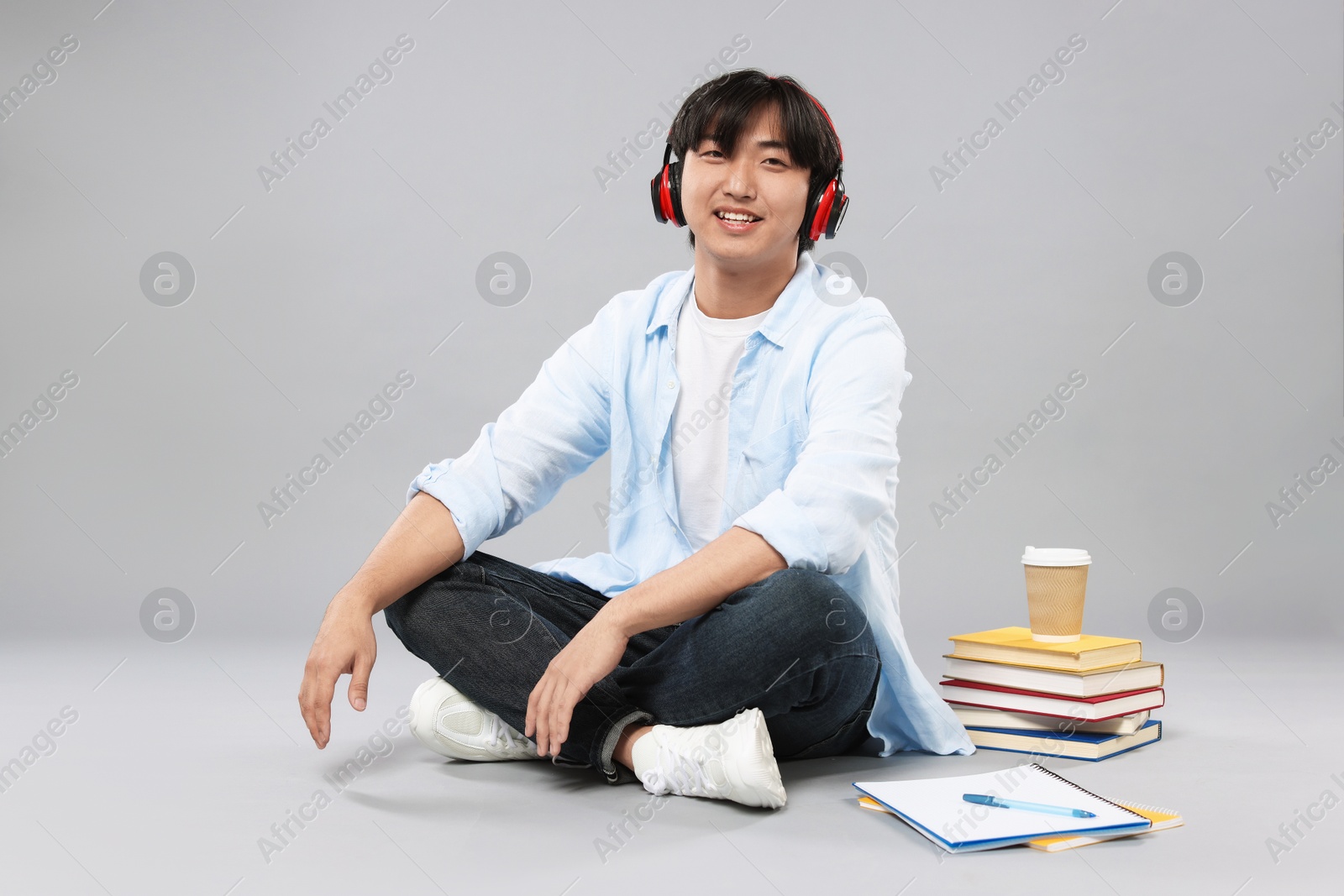Student with headphones, books and coffee on grey background Photo of Student with headphones, books and coffee on grey background
