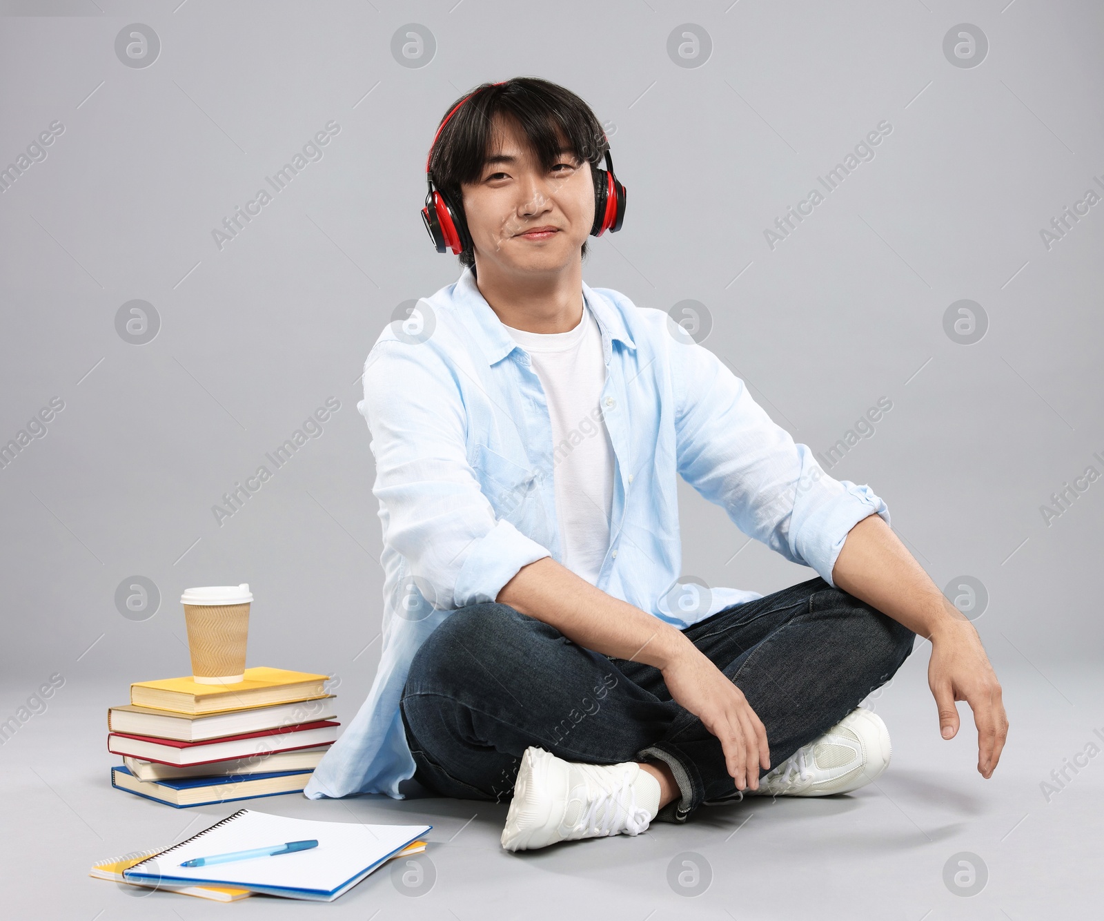 Student with headphones, books and coffee on grey background Photo of Student with headphones, books and coffee on grey background