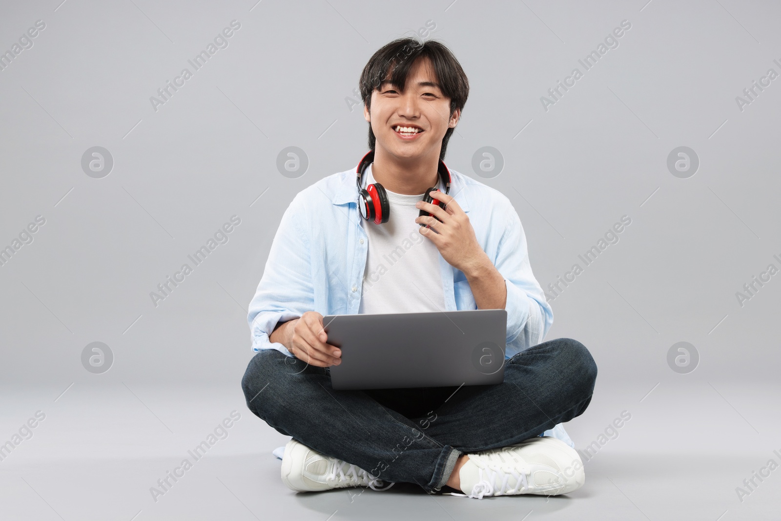 Student with headphones and laptop on grey background Photo of Student with headphones and laptop on grey background