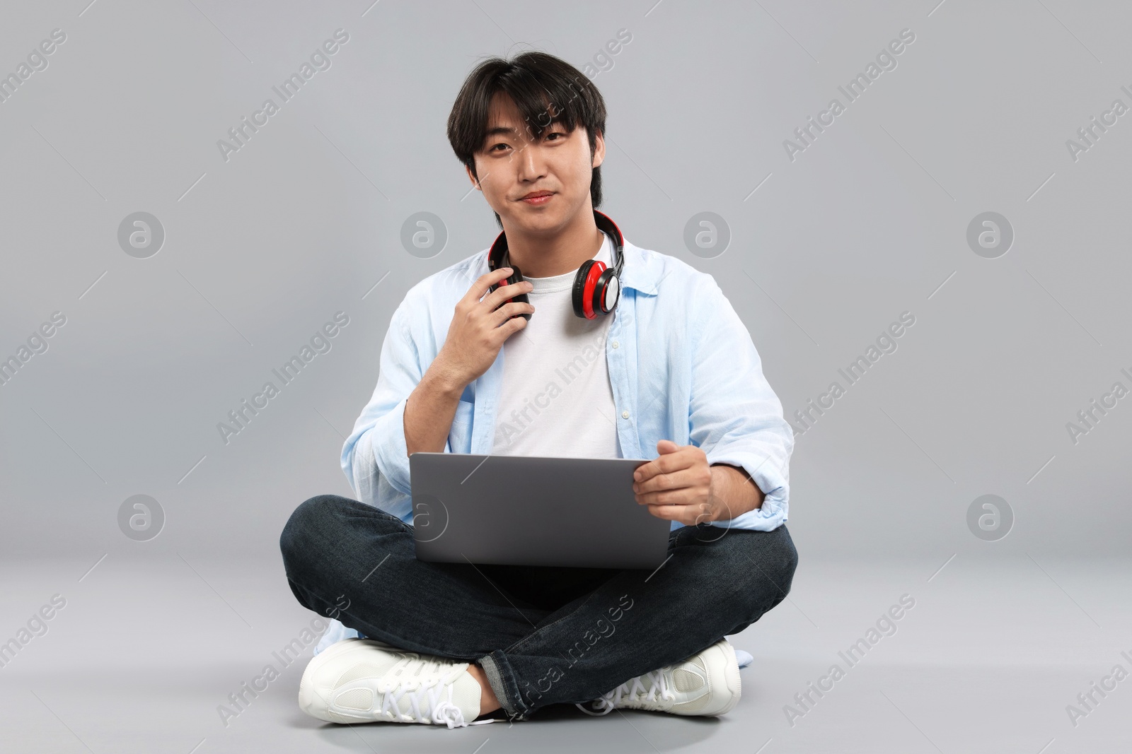Student with headphones and laptop on grey background Photo of Student with headphones and laptop on grey background