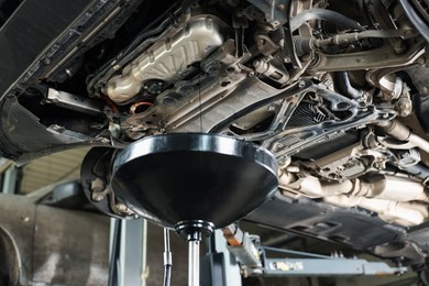 Photo of Dirty old motor oil dripping from car engine into container in workshop, closeup