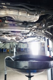 Photo of Dirty old motor oil dripping from car engine into container in workshop, closeup