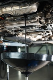 Photo of Dirty old motor oil dripping from car engine into container in workshop, closeup