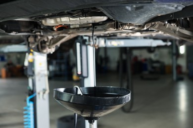 Photo of Dirty old motor oil dripping from car engine into container in workshop, closeup
