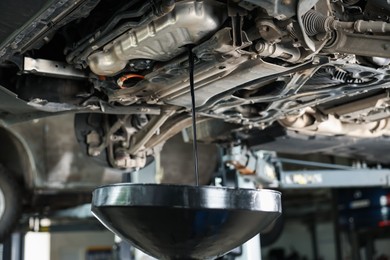 Photo of Dirty old motor oil dripping from car engine into container in workshop, closeup