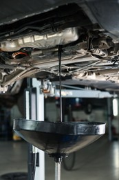 Photo of Dirty old motor oil dripping from car engine into container in workshop, closeup
