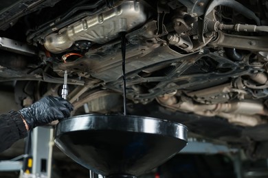 Photo of Worker removing dirty old motor oil from car engine, closeup