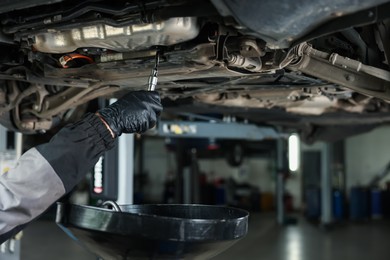 Photo of Worker removing dirty old motor oil from car engine, closeup