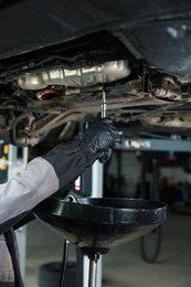 Photo of Worker removing dirty old motor oil from car engine, closeup