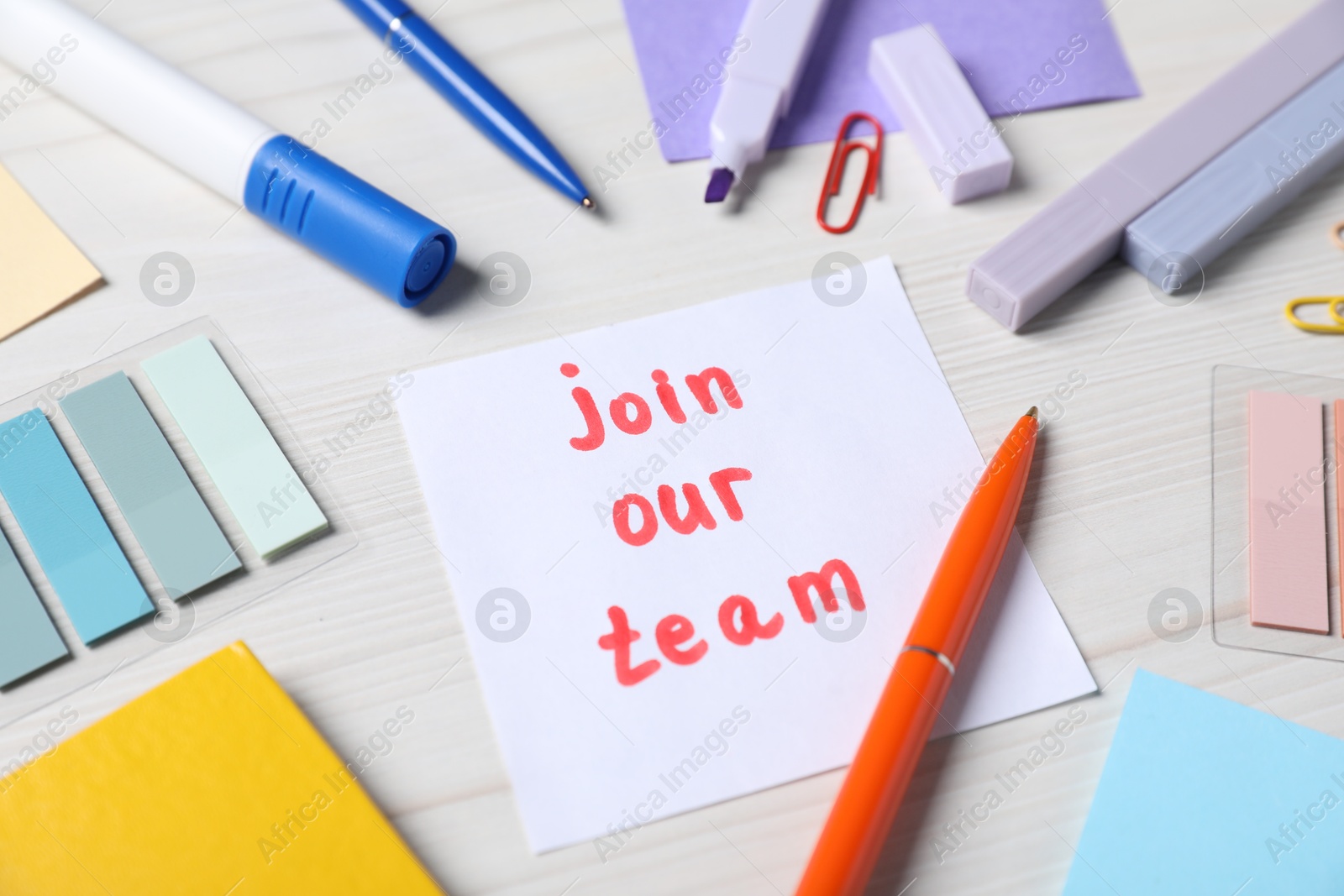 Photo of Paper note with phrase Join Our Team and stationery on white wooden table, closeup