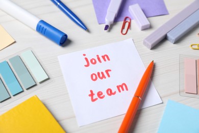 Photo of Paper note with phrase Join Our Team and stationery on white wooden table, closeup