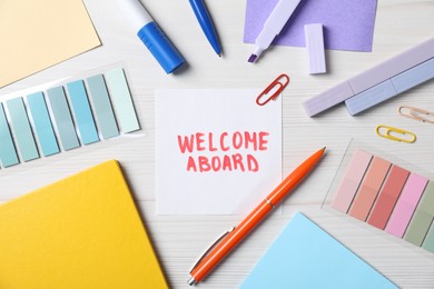Photo of Paper note with phrase Welcome Aboard and stationery on white wooden table, flat lay