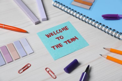 Photo of Paper note with phrase Welcome To The Team and stationery on white wooden table, closeup
