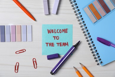 Photo of Paper note with phrase Welcome To The Team and stationery on white wooden table, flat lay