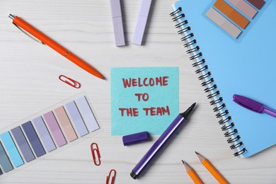 Photo of Paper note with phrase Welcome To The Team and stationery on white wooden table, flat lay