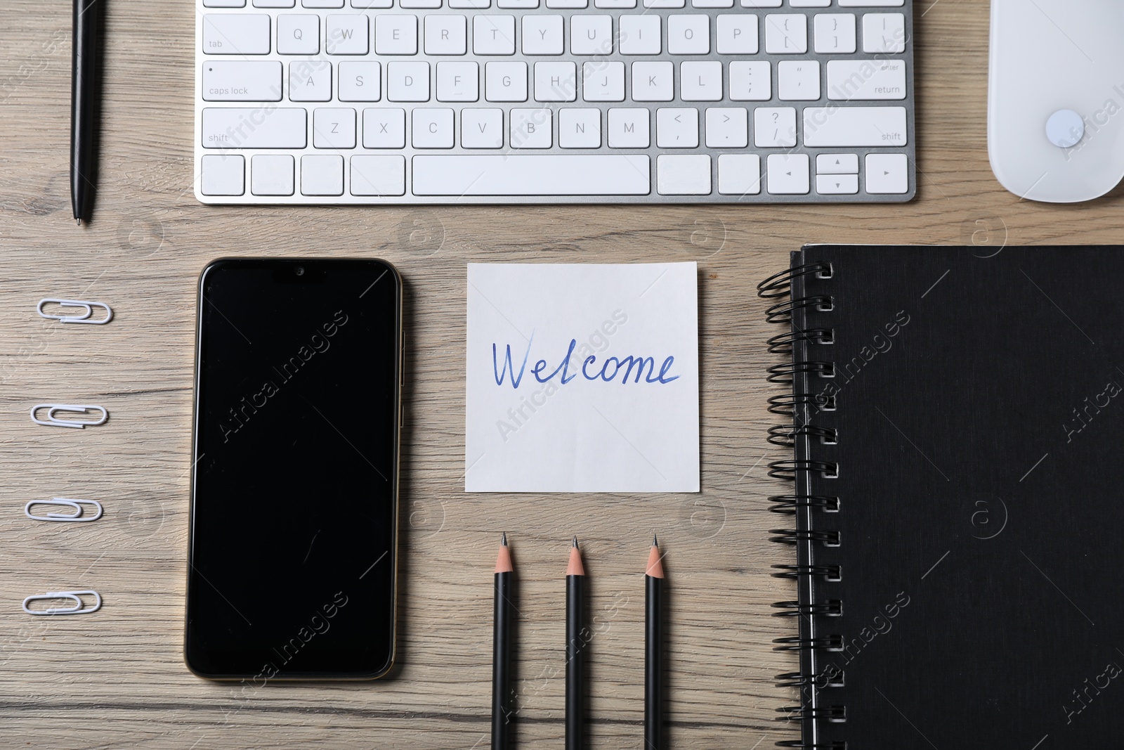 Paper note with word Welcome, smartphone, keyboard and stationery on wooden table, flat lay Photo of Paper note with word Welcome, smartphone, keyboard and stationery on wooden table, flat lay