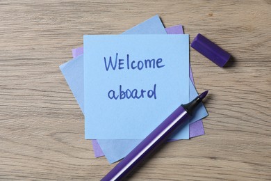 Photo of Paper note with phrase Welcome Aboard and felt tip pen on wooden table, top view