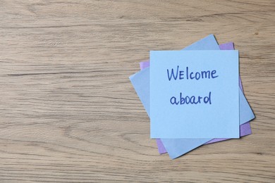 Photo of Paper note with phrase Welcome Aboard on wooden table, top view. Space for text