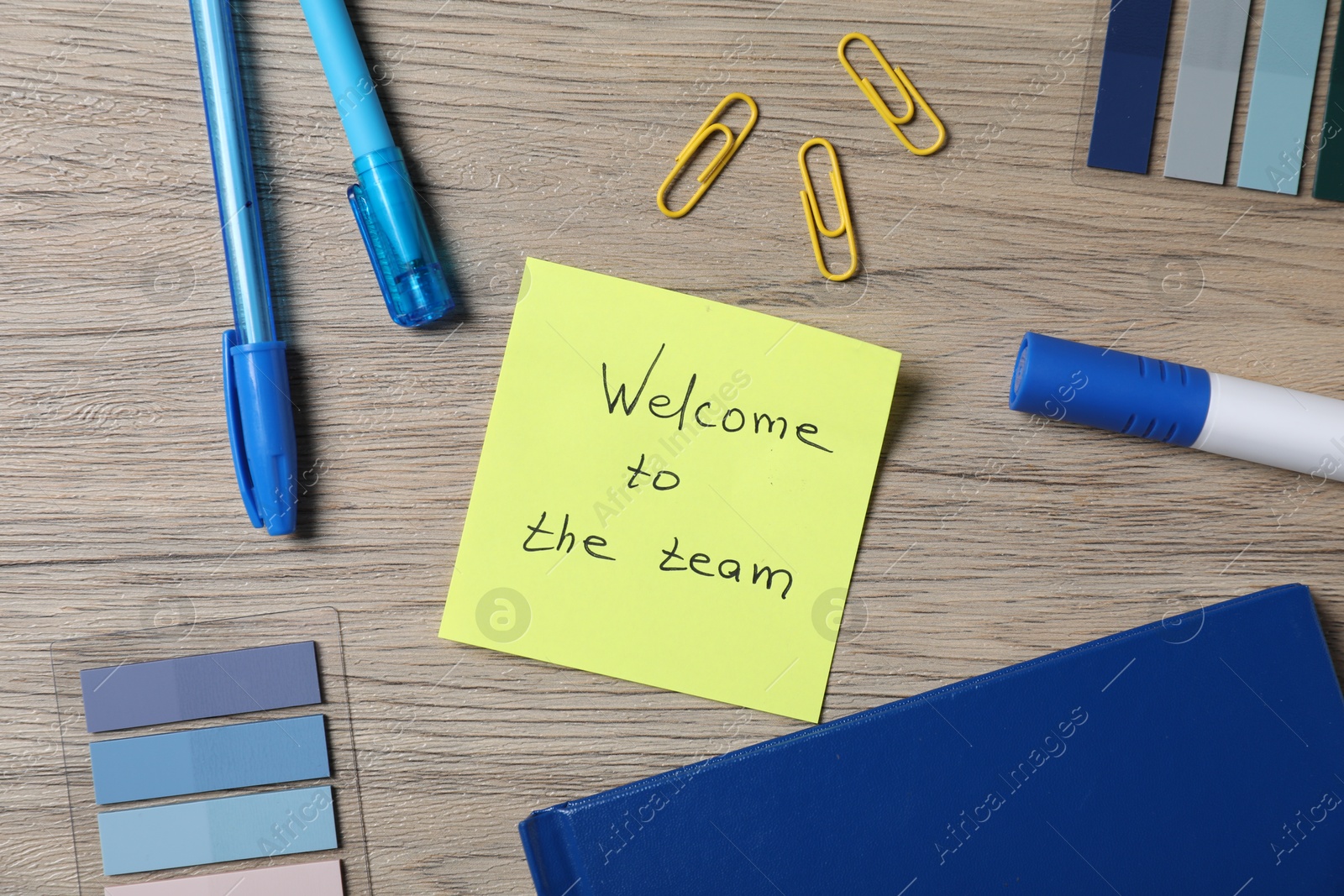 Photo of Paper note with phrase Welcome To The Team and stationery on wooden table, flat lay