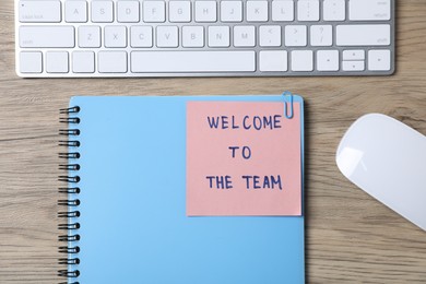 Photo of Paper note with phrase Welcome To The Team, keyboard and stationery on wooden table, flat lay