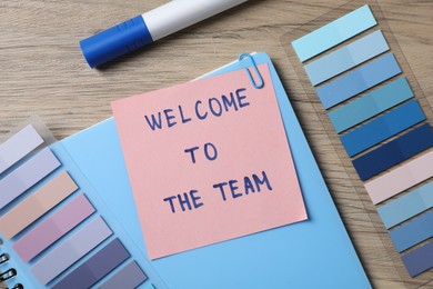 Photo of Paper note with phrase Welcome To The Team and stationery on wooden table, flat lay