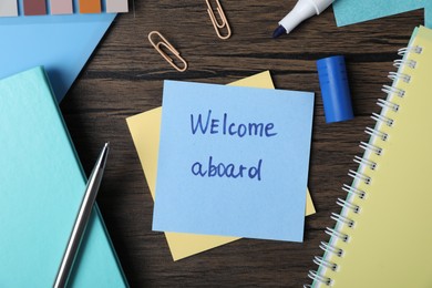 Photo of Paper note with phrase Welcome Aboard and stationery on wooden table, flat lay