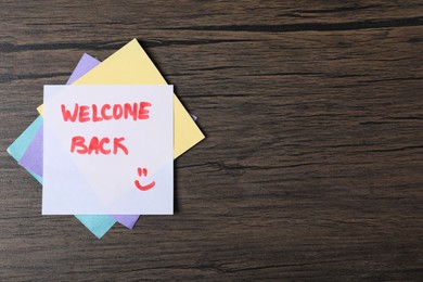 Photo of Paper note with phrase Welcome Back on wooden table, top view. Space for text