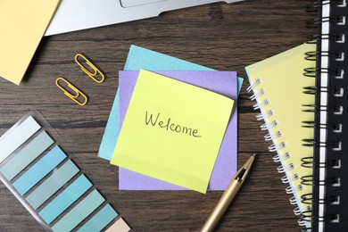 Photo of Paper note with word Welcome and stationery on wooden table, flat lay