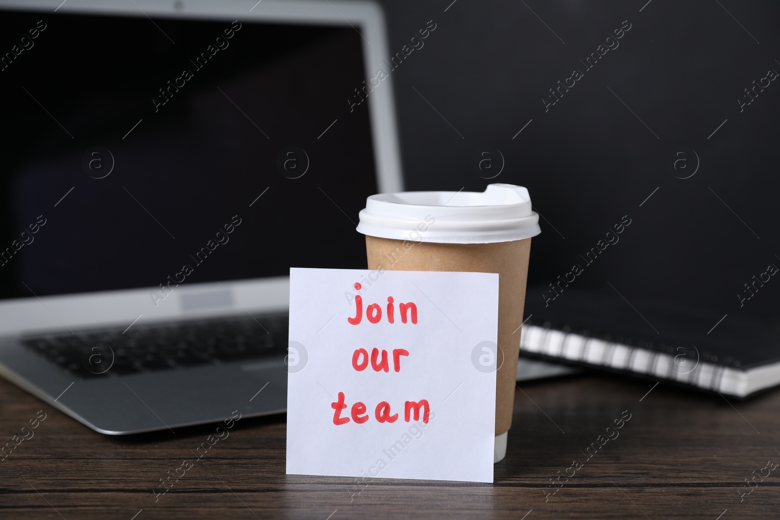 Paper note with phrase Join Our Team, cup of coffee, laptop and notebook on wooden table Photo of Paper note with phrase Join Our Team, cup of coffee, laptop and notebook on wooden table