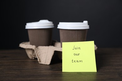 Photo of Paper note with phrase Join Our Team and cups of coffee on wooden table