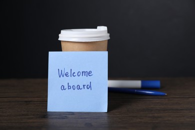 Photo of Paper note with phrase Welcome Aboard, cup of coffee and stationery on wooden table