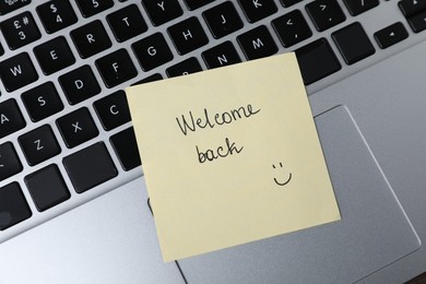 Photo of Paper note with phrase Welcome Back on laptop, closeup