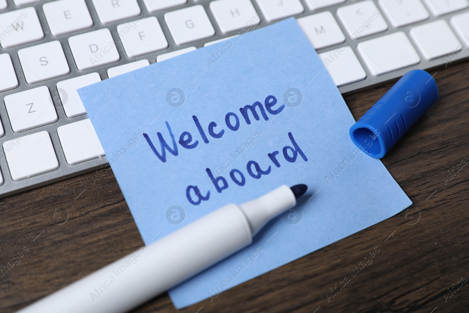 Paper note with phrase Welcome Aboard, marker and keyboard on wooden table, closeup Photo of Paper note with phrase Welcome Aboard, marker and keyboard on wooden table, closeup